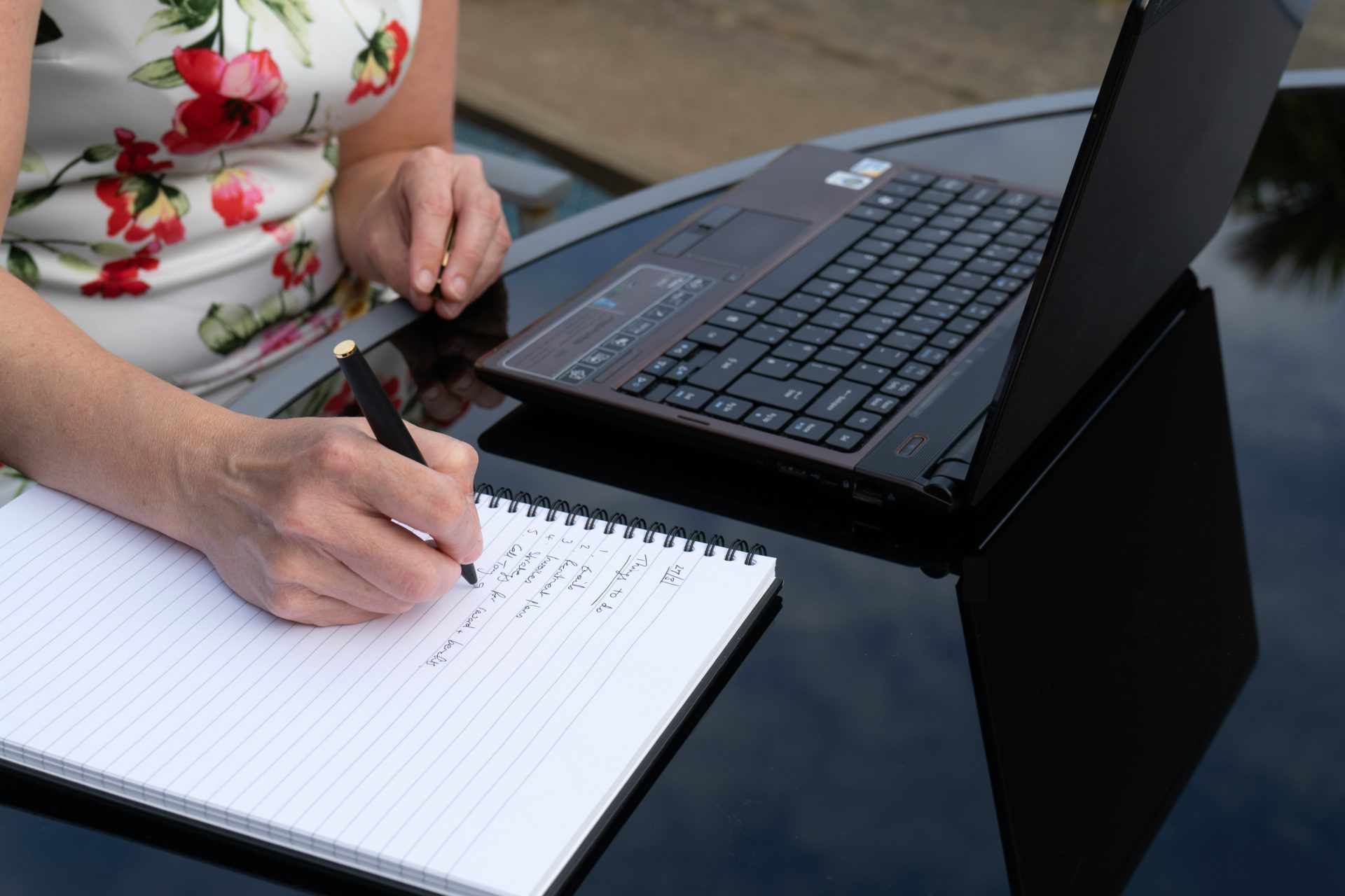 une personne qui écrit sur un morceau de papier à côté d'un ordinateur portable